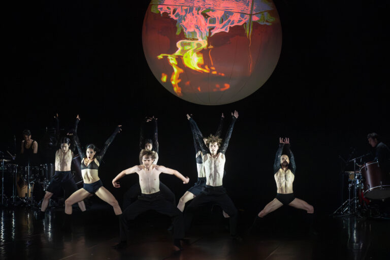 Dansers in zware kostuums onder grote gekleurde bol