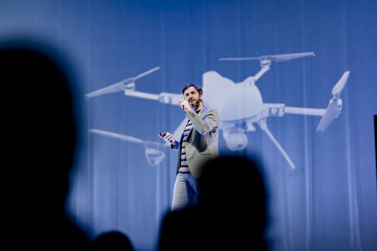 Lieven Scheire in pak met een afbeelding van een drone