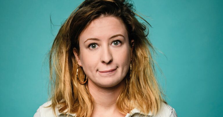 Een vrouw met lichtbruin, schouderlang haar met een blonde ombre, die een neutrale gezichtsuitdrukking heeft voor een turquoise achtergrond.