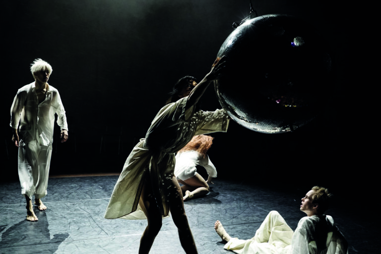 Vier dansers op het podium waarvan één een grote discobal pakt