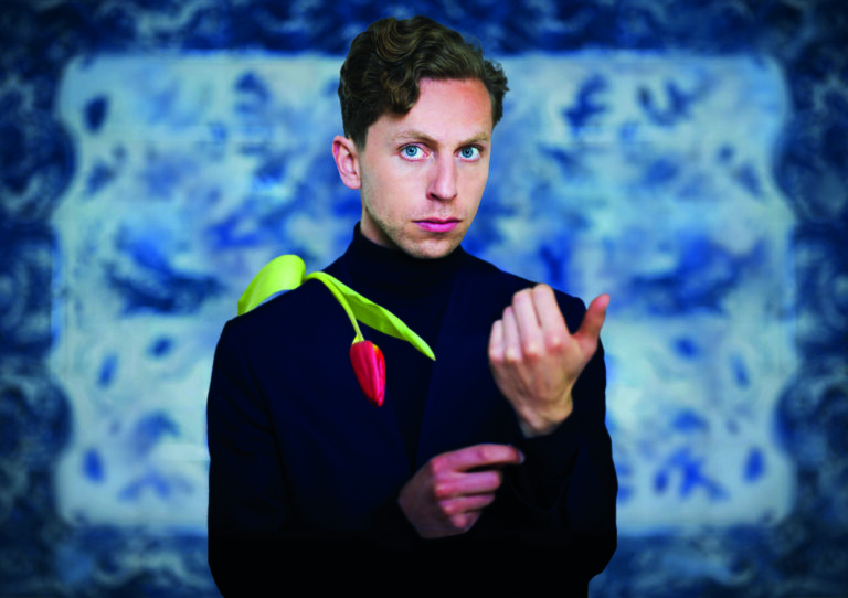 Portretfoto van Boban Benjamin in een zwarte trui met een roos op zijn schouder.