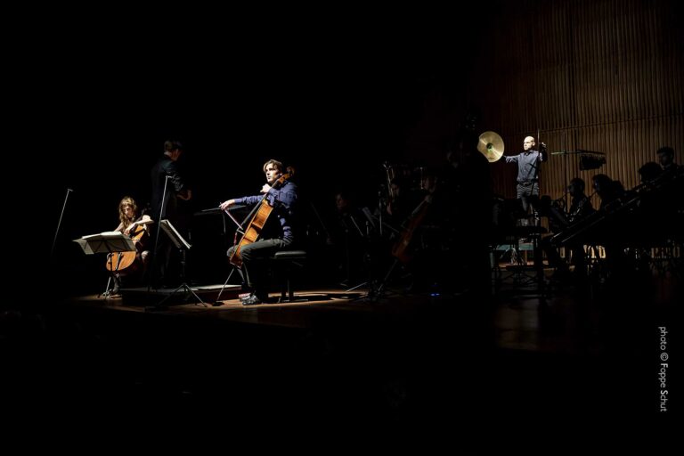 Een groep muzikanten speelt op een podium in een donker auditorium.