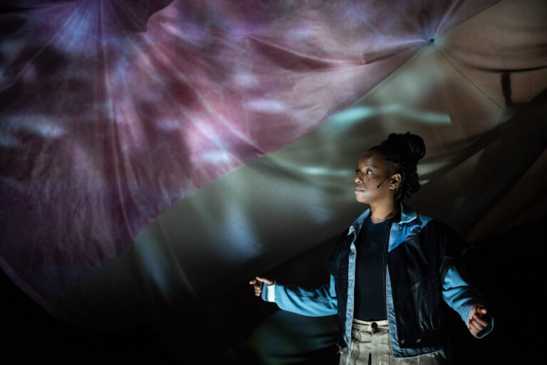 Een persoon staat onder kleurrijke lichtprojecties in een donkere omgeving.