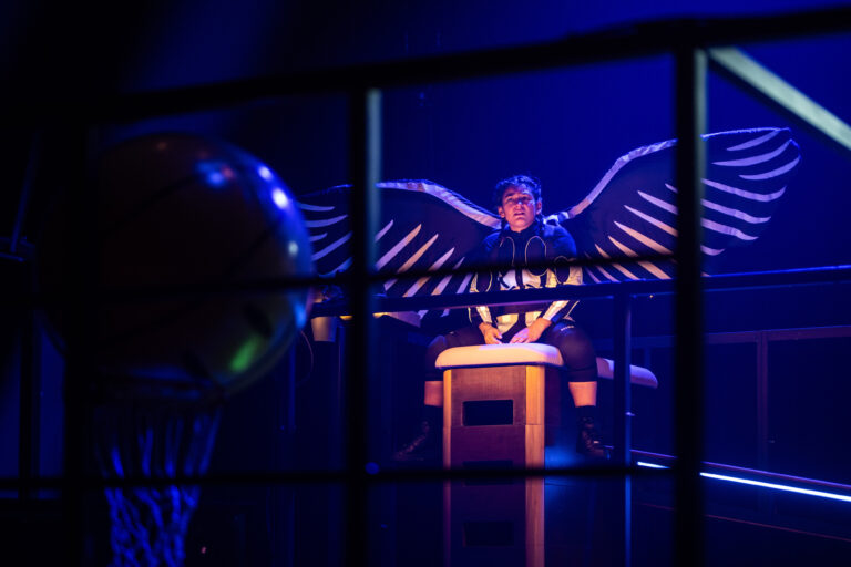 Donkere sporthal met gymtoestellen met jongen op kast met vleugels