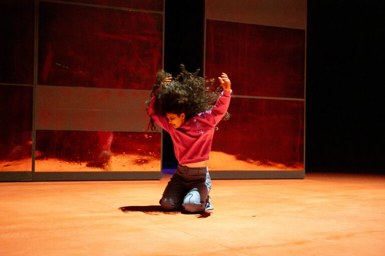 Actrice van HEAT met langere donkere krullen op haar knieën op de grond