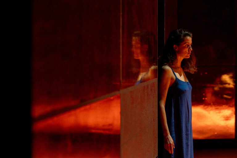 Actrice in een blauwe jurk leunt met haar rug tegen een spiegel