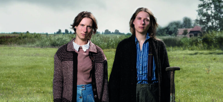 Twee jonge mensen staan zijdelings naar de camera met een landelijke achtergrond vol groen.