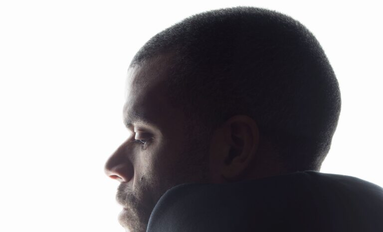 Profiel van een man met een scherp gedefinieerde kaaklijn, zichtbaar tegen een lichte achtergrond.