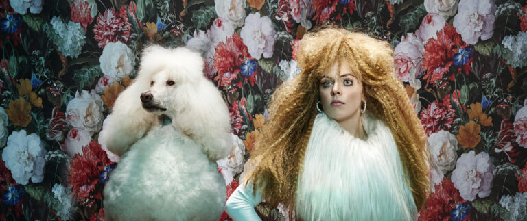 Lisa Ostermann met een witte poedel voor een bloemenmuur