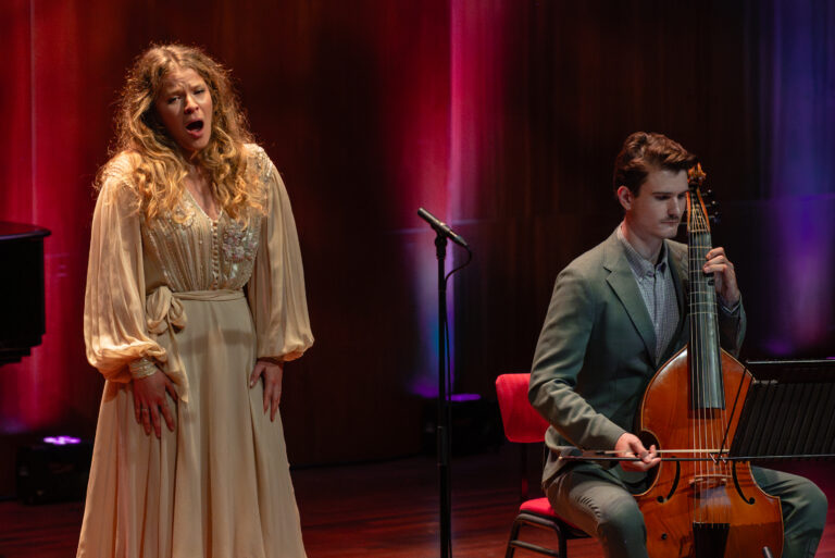 vrouw zingt naast een man met cello voor een rode achtergrond