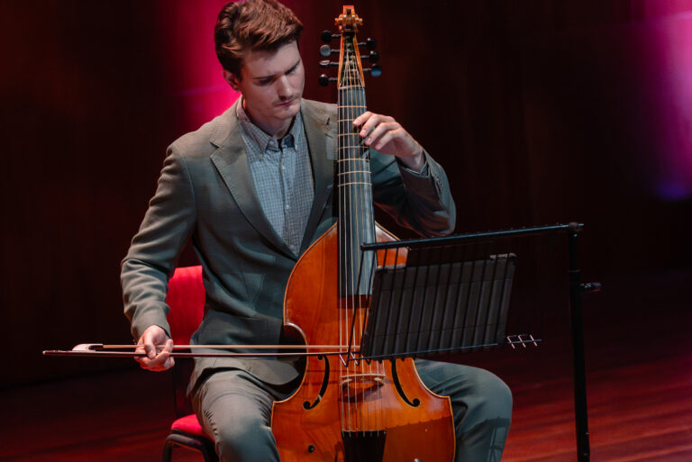 man met cello voor rode achtergrond in pak