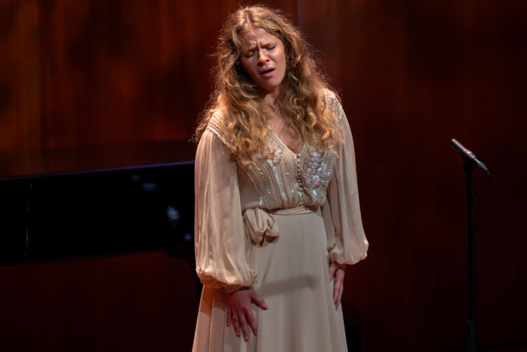 Vrouw in witte jurk zingt en staat voor rode achtergrond