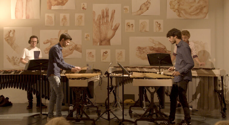 Twee muzikanten spelen op marimba's voor een achtergrond van handtekeningen en illustraties van handen.