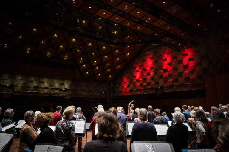 een groep mensen van het kamerkoor kijkt naar de dirigent
