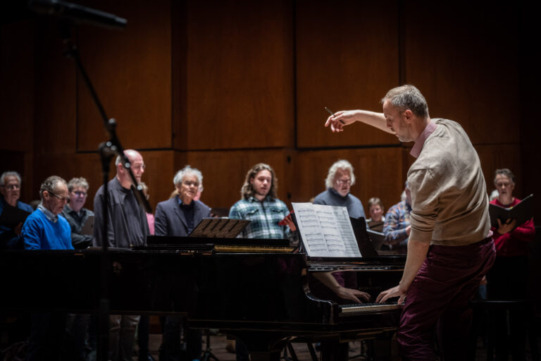de dirigent staat voor de piano en heeft een hand in de lucht