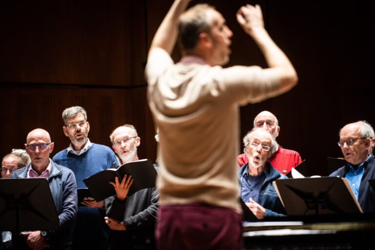 Een deel van het koor aan het zingen met de dirigent wazig in beeld