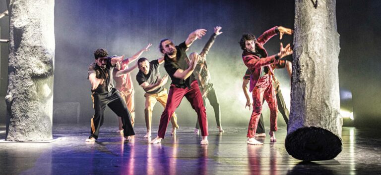Zeven dansers staan tussen boomstammen