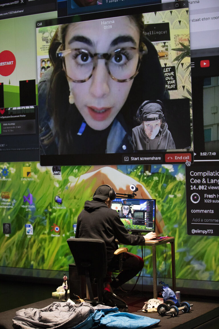 Een persoon zit achter een computer terwijl ze interactie heeft met een grote video van een andere persoon op een scherm.