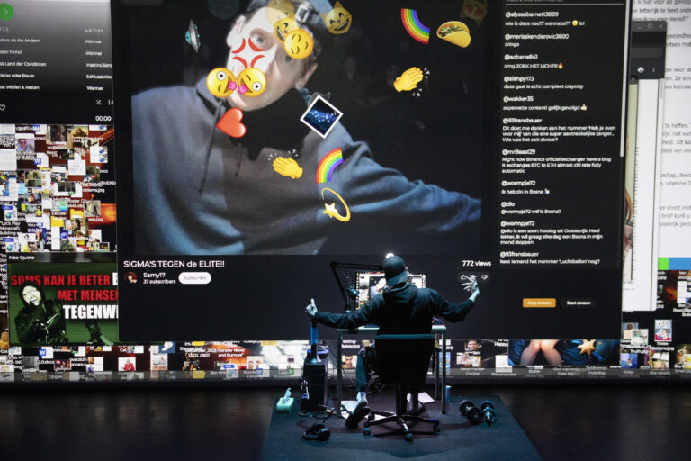 Een persoon zit achter een computer, met een groot projectiescherm waarop emoticons en afbeeldingen zijn weergegeven.