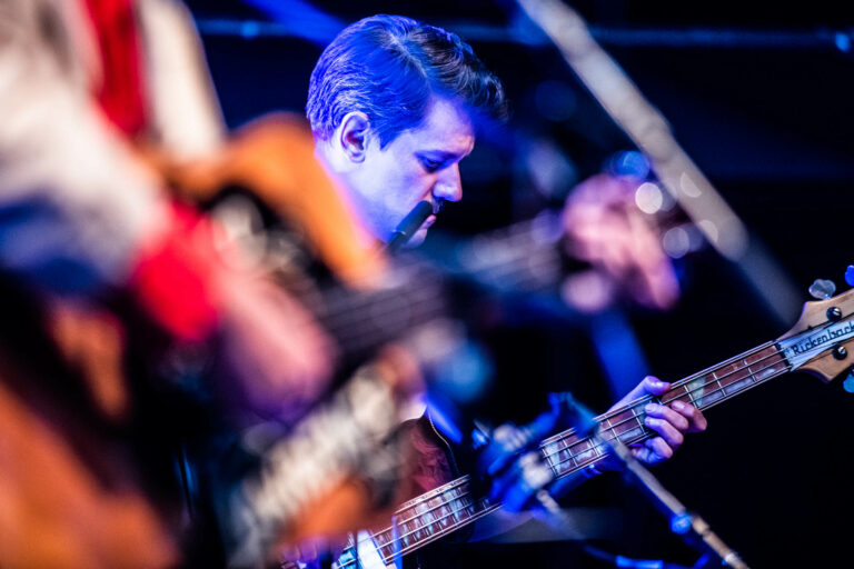 Een muzikant speelt gitaar op een podium met een focus op zijn geconcentreerde gezicht en de instrumenten op de voorgrond.