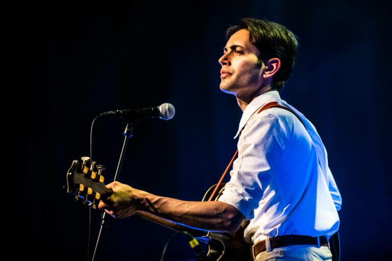 Een muzikant speelt gitaar en zingt op een podium met een microfoon.