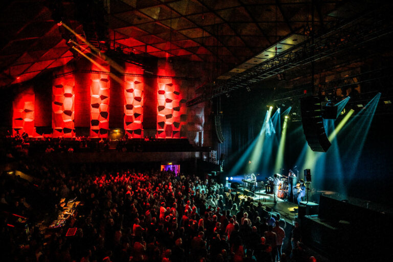 Een druk bezocht concert in een sfeervolle zaal met kleurrijke verlichting.