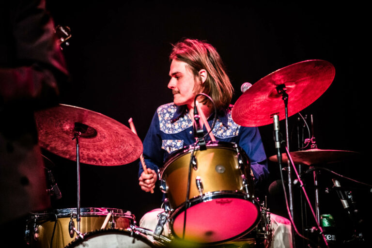 Een drummer speelt op een drumstel met felgekleurde bekken op een podium.
