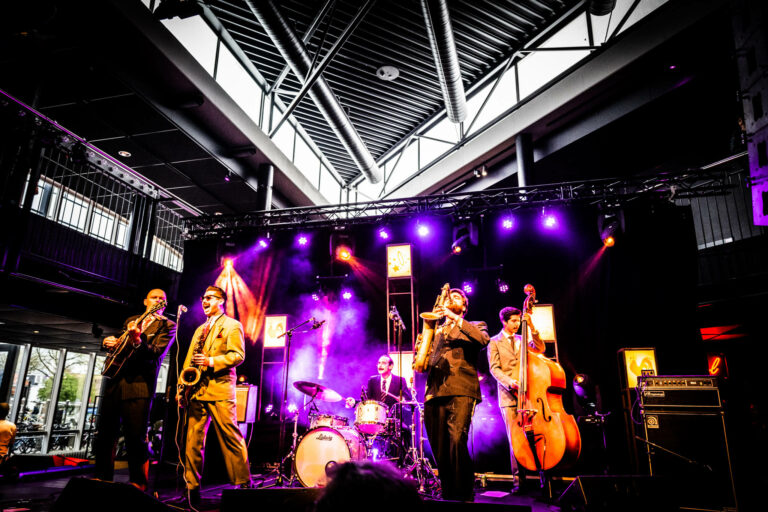 Een band speelt live muziek op een podium, omringd door kleurrijke lichten.