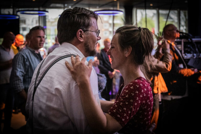 Een man en een vrouw dansen innig samen in een drukke, sfeervolle setting.