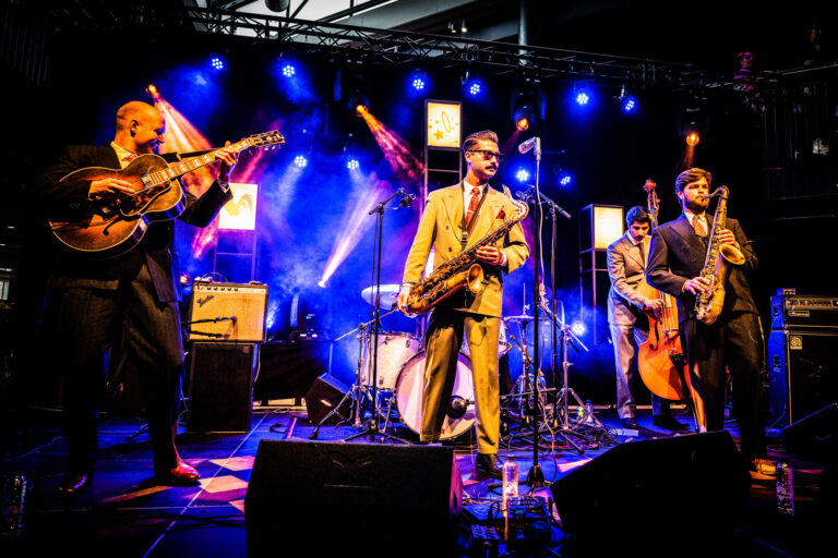 Een jazzband speelt op een podium, omringd door kleurrijke lichten.