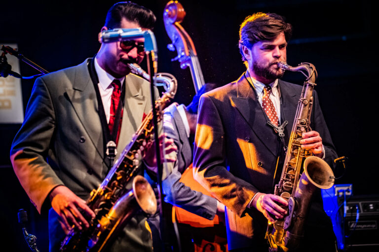 Twee muzikanten spelen op hun saxofonen tijdens een live jazzoptreden.