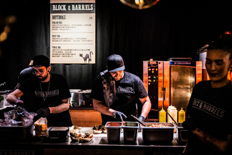 Twee koks bereiden maaltijden aan een werktafel met verschillende ingrediënten en een menu op de achtergrond.