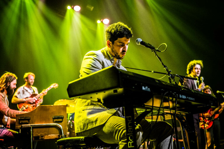 Een muzikant speelt keyboards op een podium, omgeven door groene verlichting.