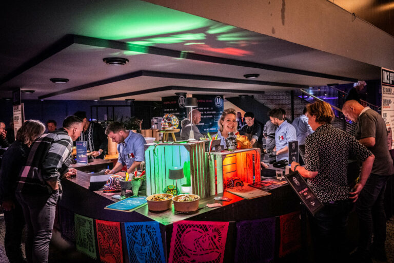 Een drukke barsetting met kleurrijke verlichting en mensen die drankjes en gerechten bereiden.