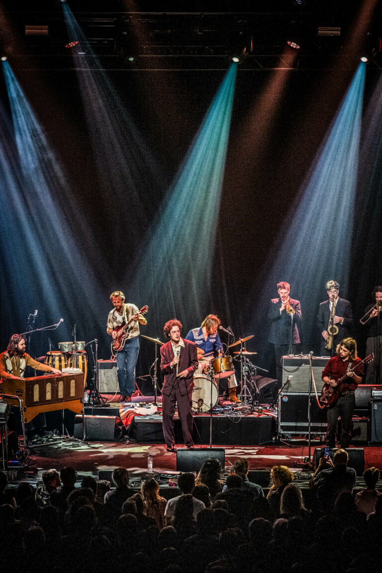 Een band speelt live op het podium met verschillende instrumenten en een dynamische lichtshow.