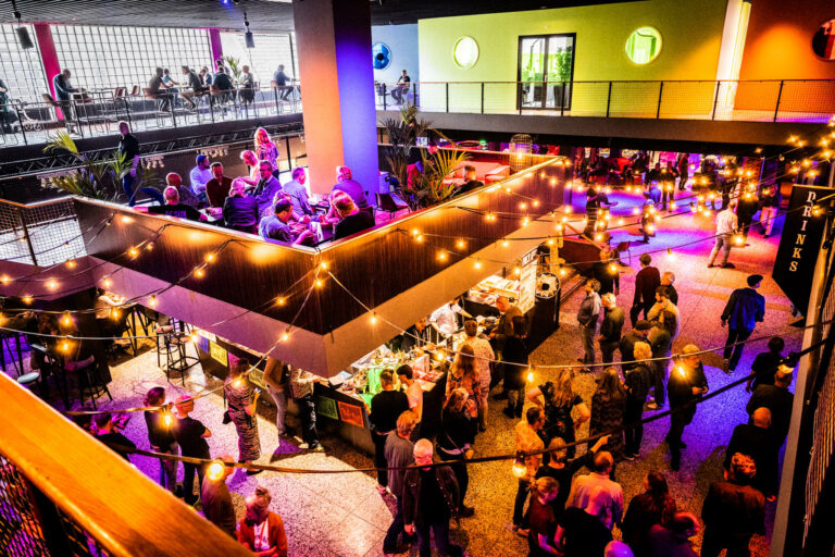 Druk bezochte horeca-ruimte met kleurrijke verlichting en mensen die socializen.