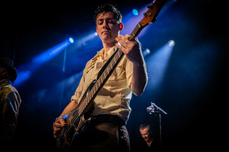 Een muzikant speelt basgitaar op een podium met blauwe verlichting.