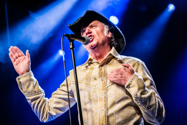 Een man in een cowboyhoed zingt gepassioneerd in een spotlight tijdens een optreden.