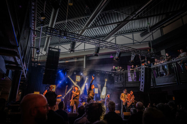Een live muziekband optredend op een podium met kleurrijke lichten en een menigte kijkers.