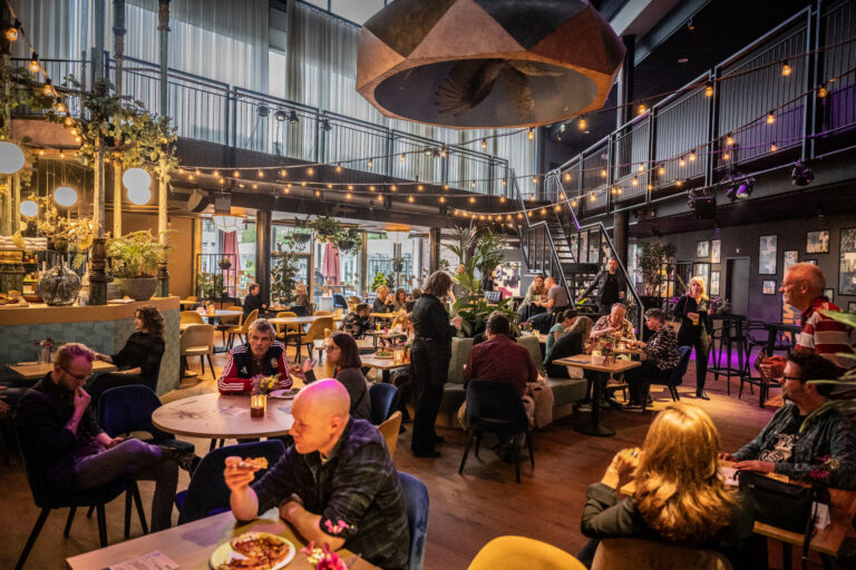 Een levendig restaurantinterieur met gasten aan tafel, sfeerverlichting en een open bovenverdieping.