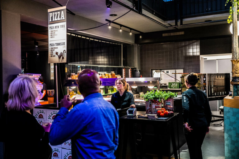 Een levendige foodstand met een menu bovenaan, waar mensen genieten van hun maaltijd in een sfeervolle omgeving.