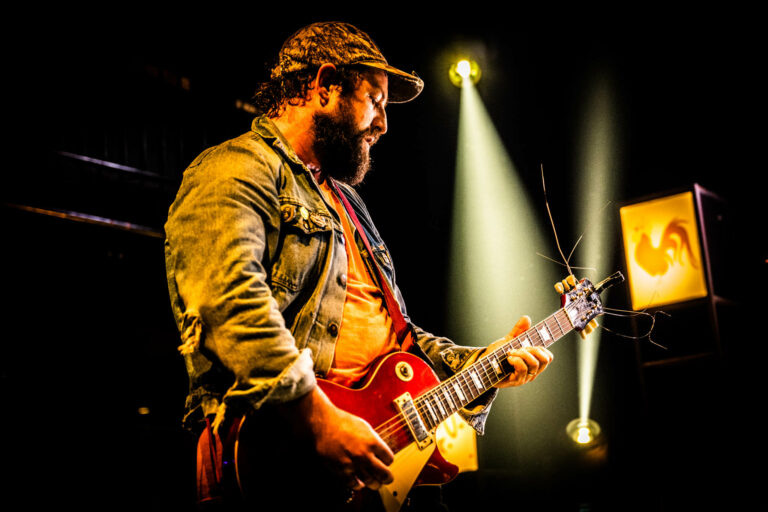 Een muzikant speelt gitaar op het podium, verlicht door lichtstralen.