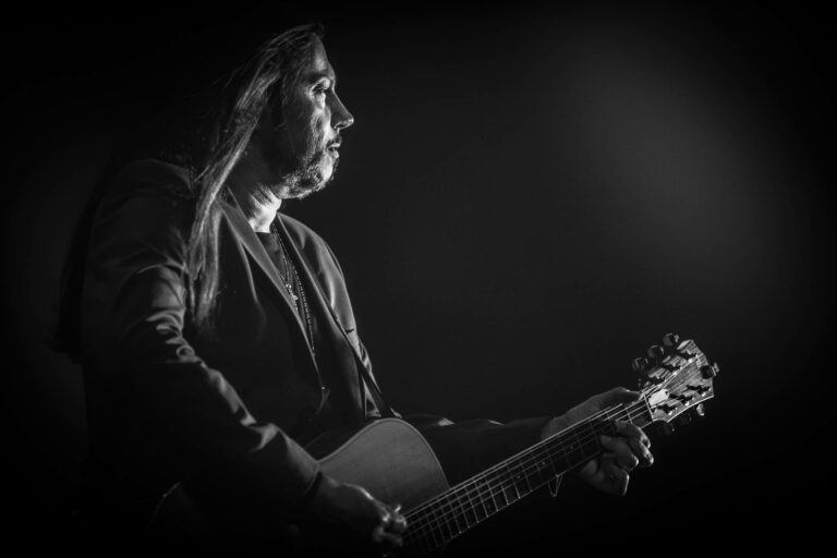 Een muzikant in zwart-wit speelt gitaar met een intense blik in de richting van het publiek.