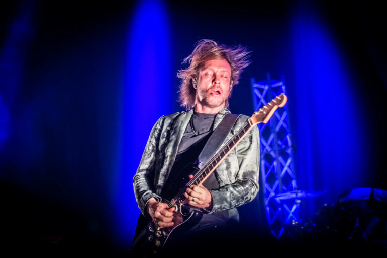 Een muzikant speelt gitaar tijdens een live optreden met blauwe verlichting.