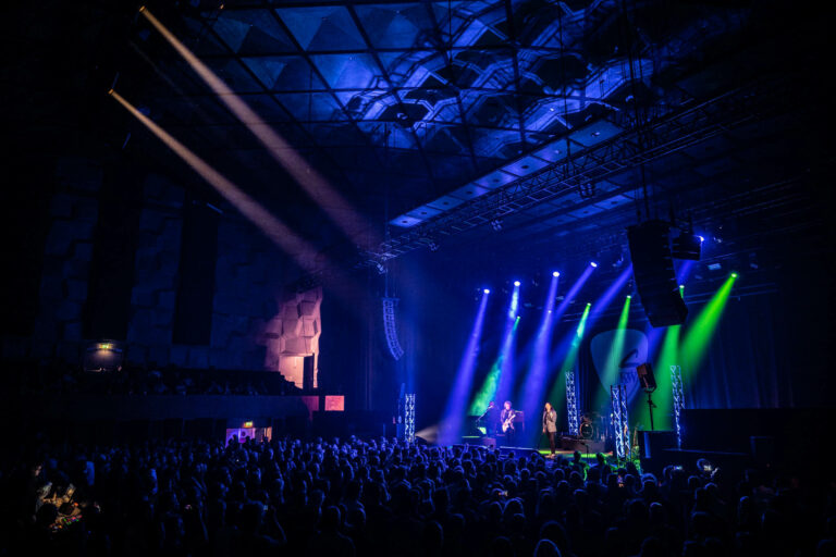 Een druk bezocht concert met kleurrijke verlichting en een podium waar muzikanten optreden.