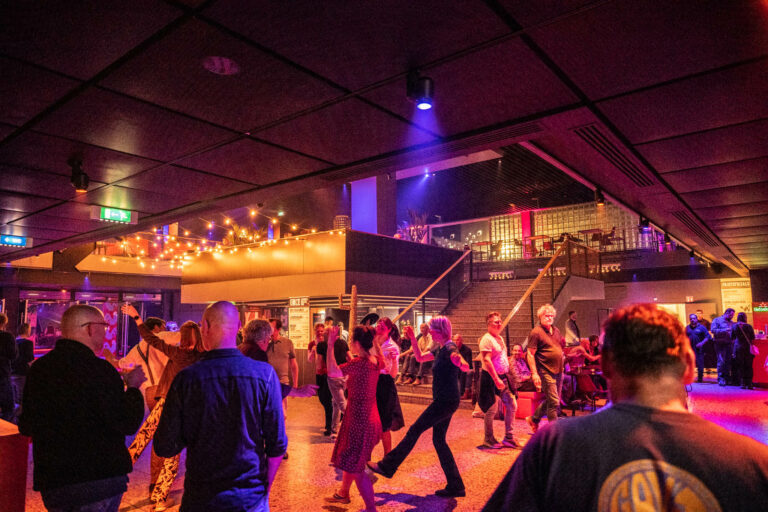 Een drukke dansvloer met mensen die vrolijk dansen onder kleurrijke verlichting.