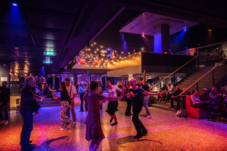 Mensen dansen op een levendig dansfeest met kleurrijke verlichting en een drukke setting.