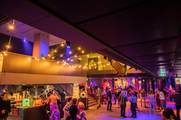 Een levendige evenementenruimte met mensen die genieten van een feest, omringd door sfeervolle verlichting en decoraties.