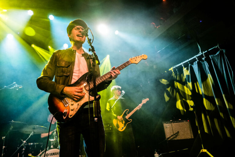 Een muzikant speelt gitaar tijdens een liveoptreden op een sfeervol verlichte podium.