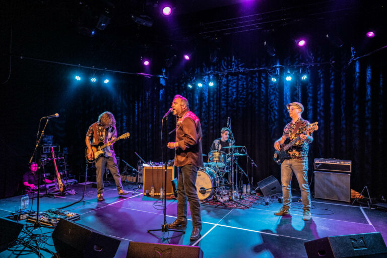 Een band speelt live op een podium met kleurrijke verlichting.